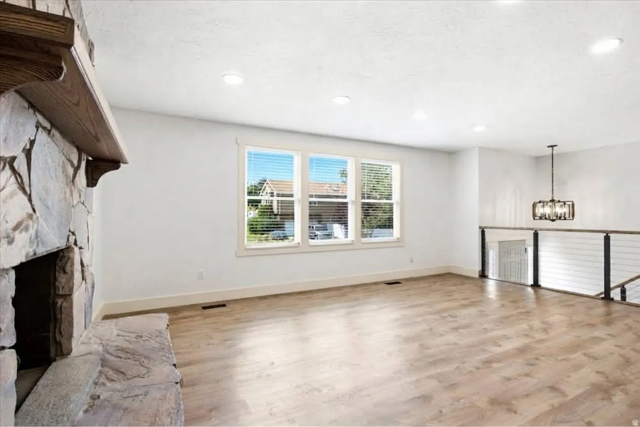 Stone fireplace with wood mantel, three-panel window, wood-finish flooring, recessed lighting, and cable railing system