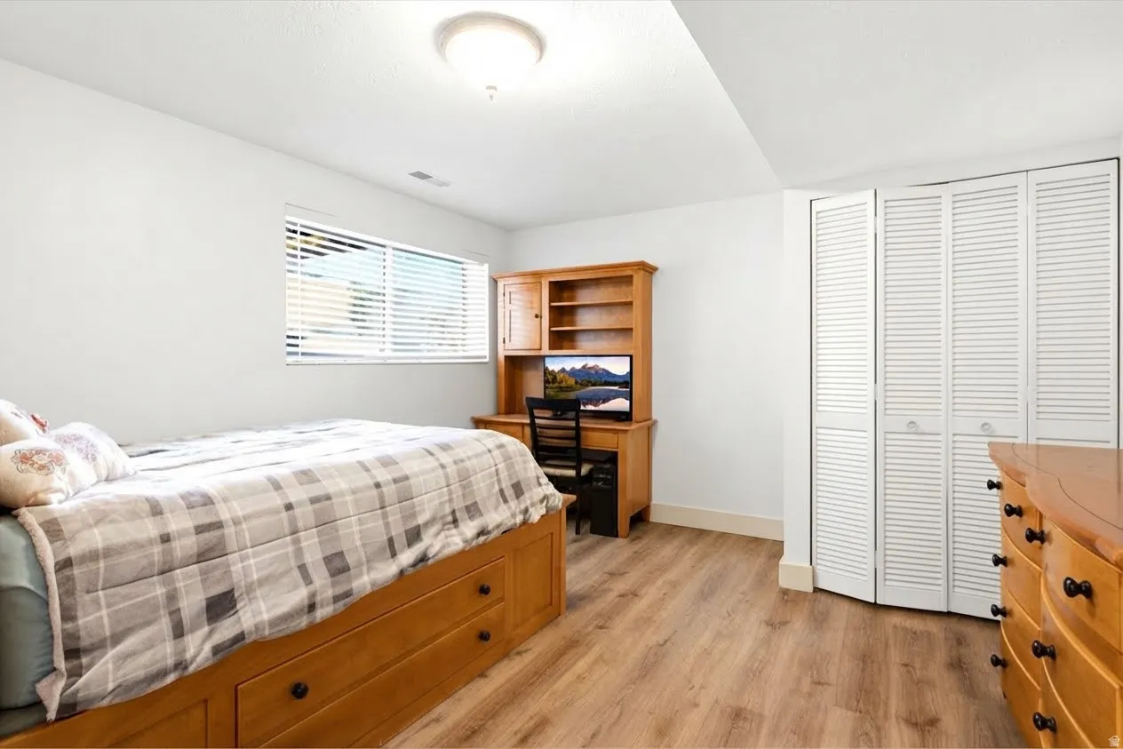 Wood-finish flooring, white louvered closet doors, window with blinds, and recessed lighting