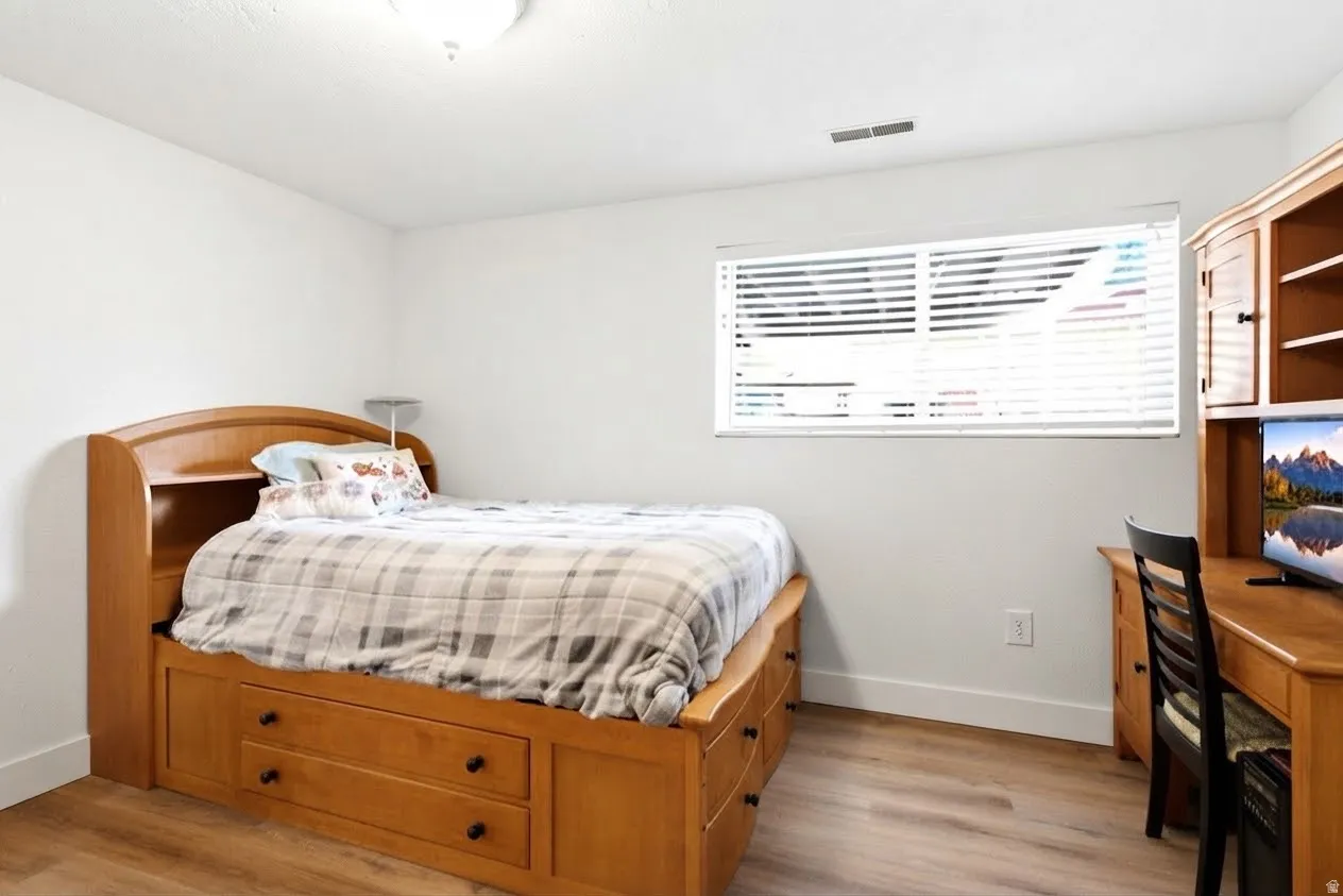 White walls with wood-finish flooring, featuring a window with horizontal blinds and a flush-mount ceiling light fixture