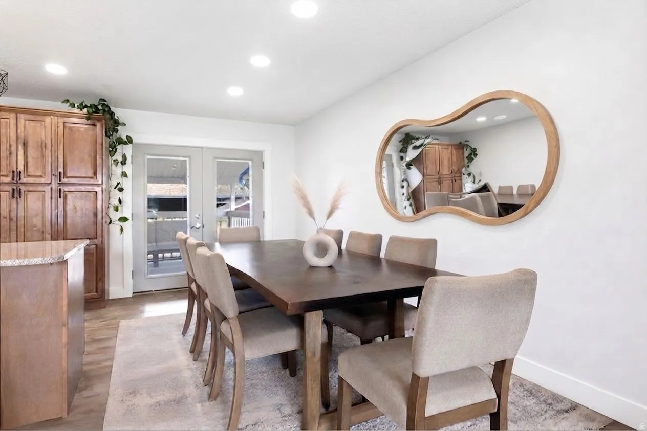 Recessed lighting illuminates the dining area featuring wood-finish flooring, a wood-framed mirror, and French doors