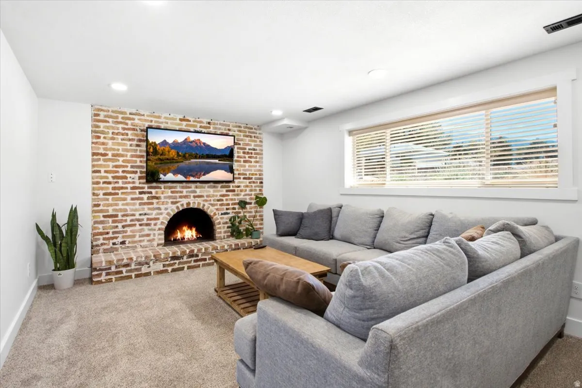 Brick accent wall with an arched firebox, wall-mounted television, recessed lighting, carpet flooring, and a large window with blinds