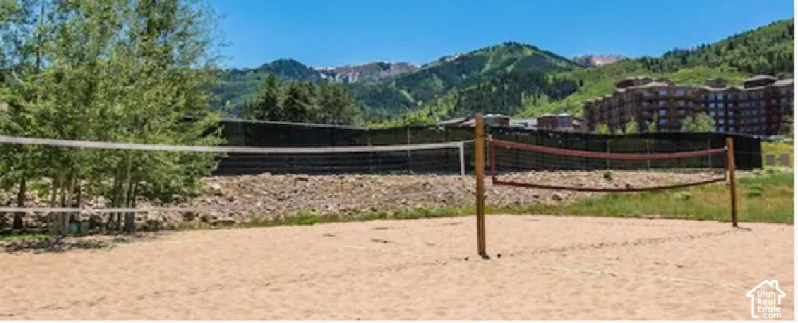 Sand volleyball court featuring wooden posts and a net, complemented by a surrounding wooded landscape and distant mountains