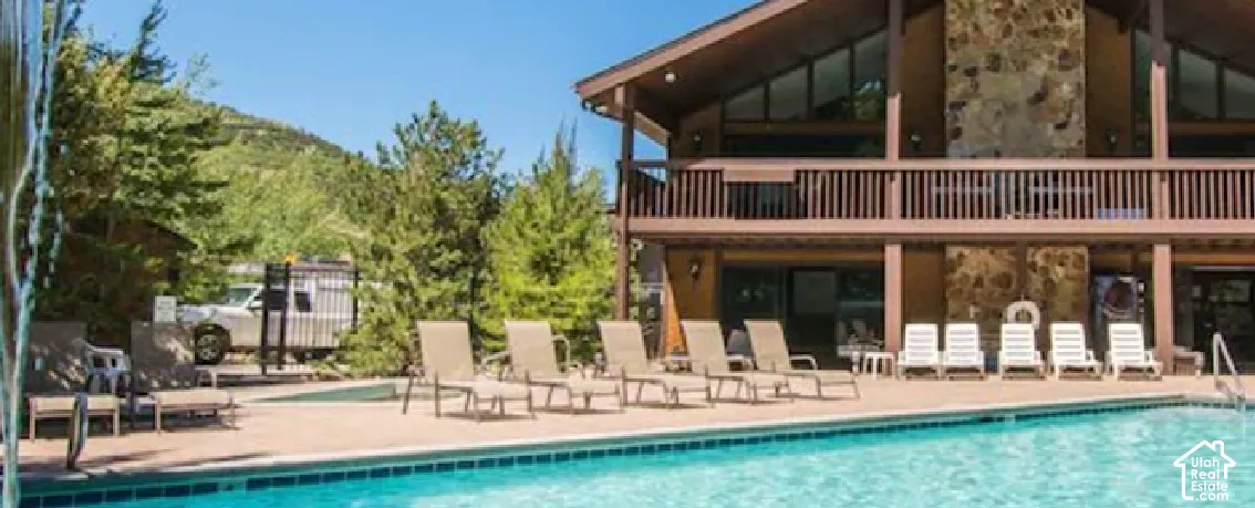 Outdoor swimming pool with a concrete deck and a multi-story building featuring stone accents and a balcony