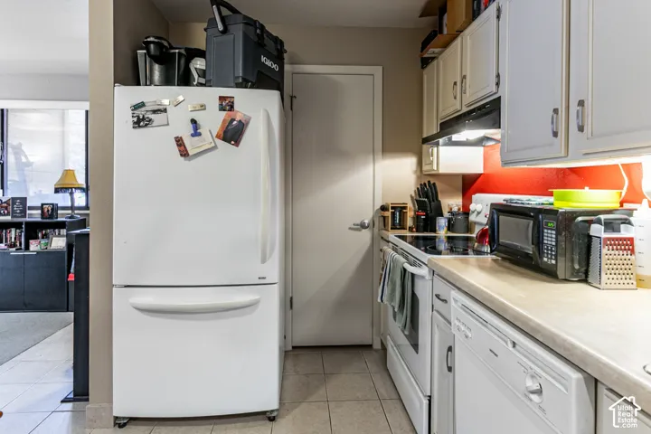 Kitchen featuring tile flooring, white cabinetry, integrated range with overhead ventilation, white dishwasher, and light-toned countertops