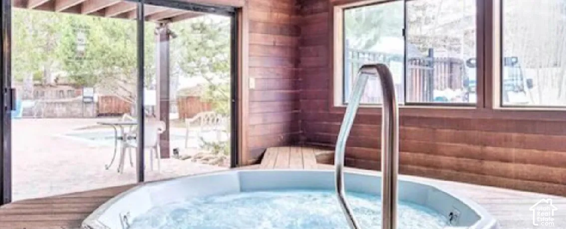 Indoor hot tub featuring a handrail, wood-paneled walls, and large windows