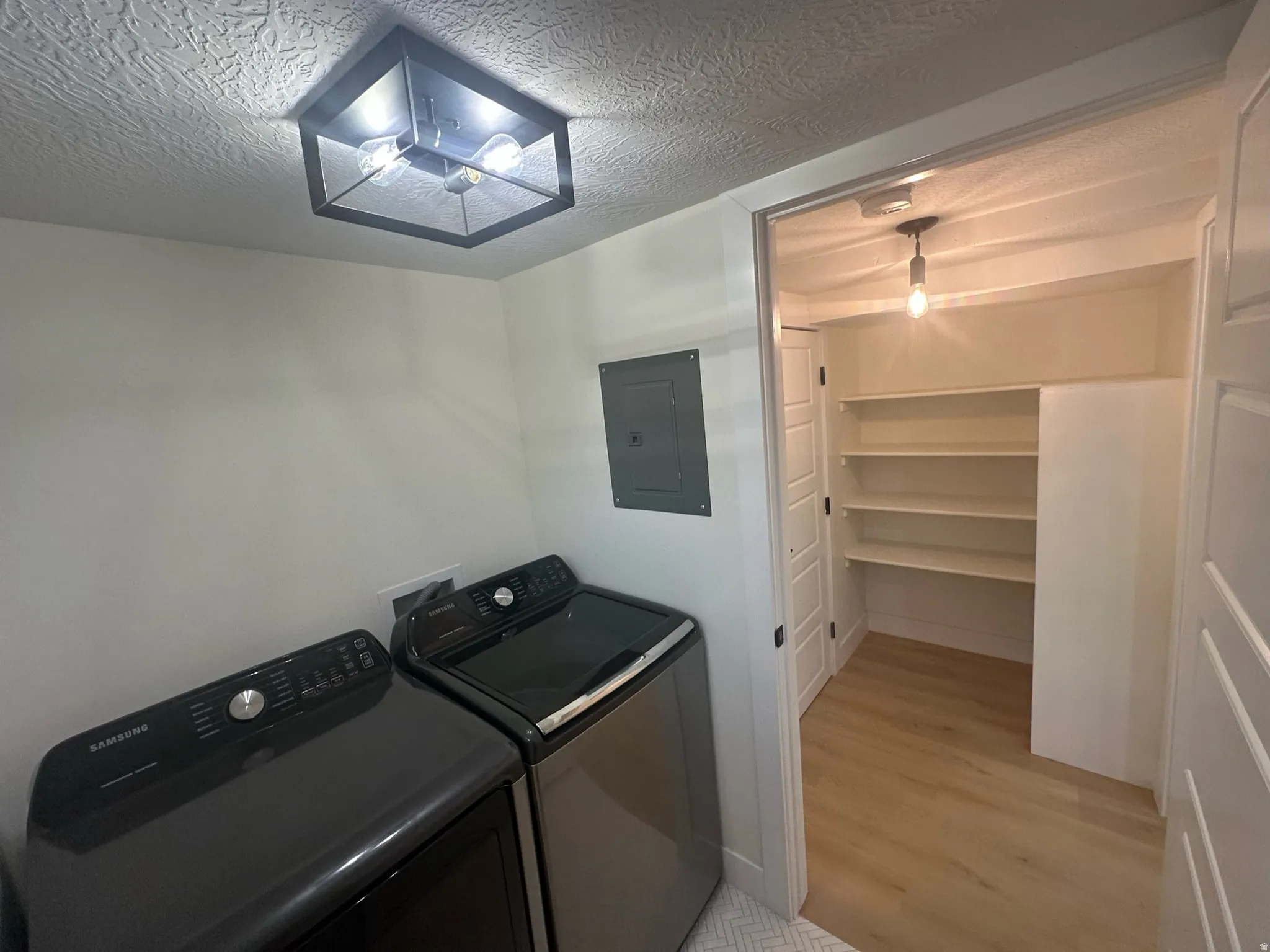Dedicated laundry area featuring a flush-mount ceiling light, light wood-finish flooring, and an adjacent storage closet with built-in shelving
