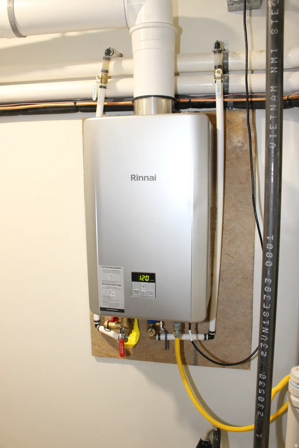 Wall-mounted Rinnai tankless water heater with digital display, visible plumbing, and gas line connections