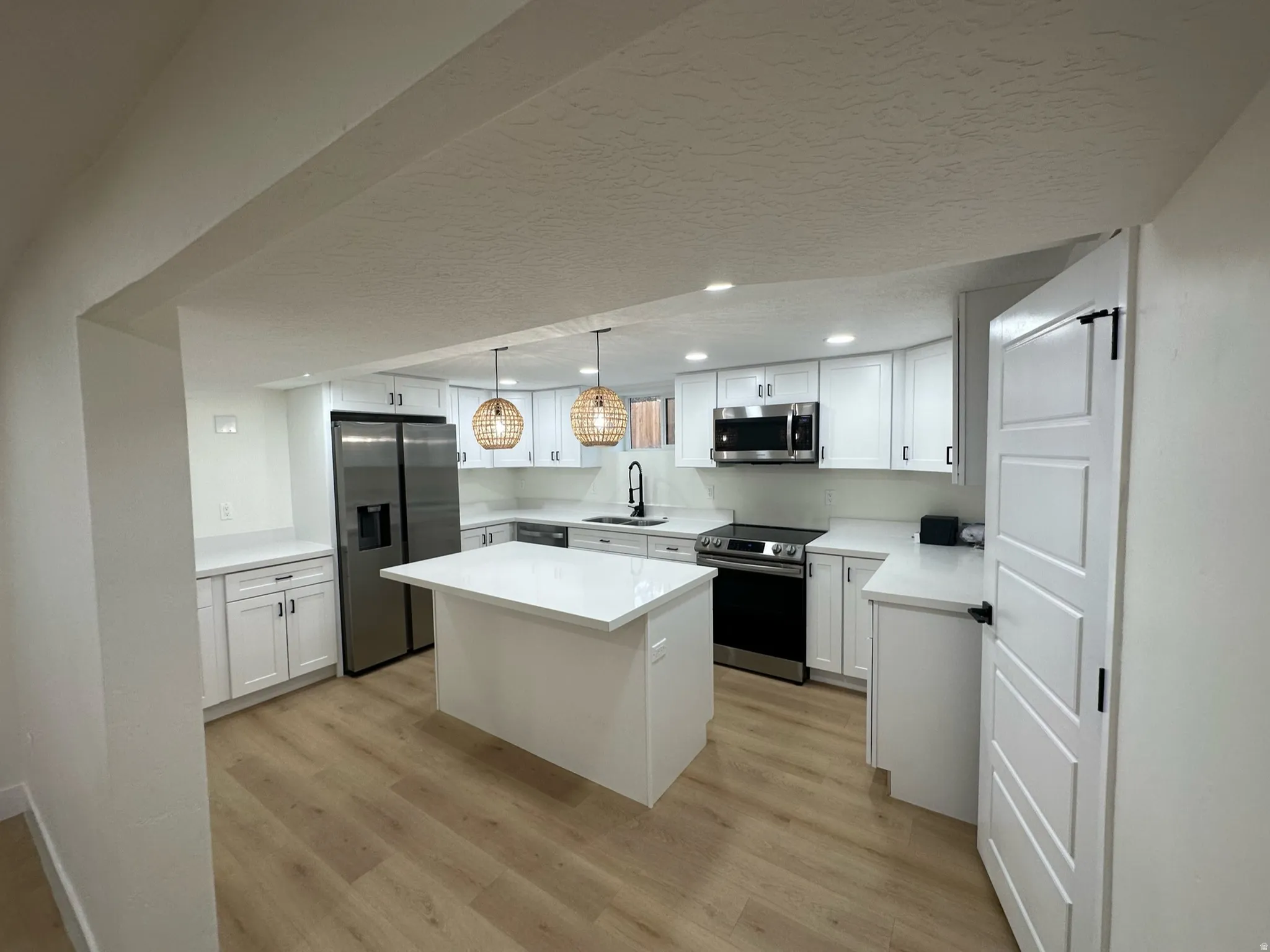 Modern kitchen featuring white cabinetry, a central island, stainless steel appliances, white countertops, and wood-finish flooring