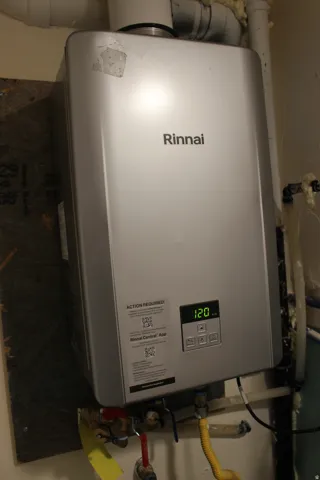 Rinnai tankless water heater with digital display, visible piping, and gas line connection