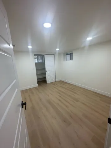 Spacious room featuring wood-finish flooring, recessed lighting, and a white paneled door with matte black hardware