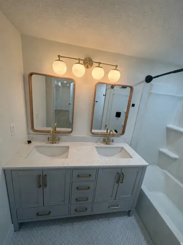 Dual vanity featuring a white countertop with integrated sinks, brass-finish fixtures a lighted sconce