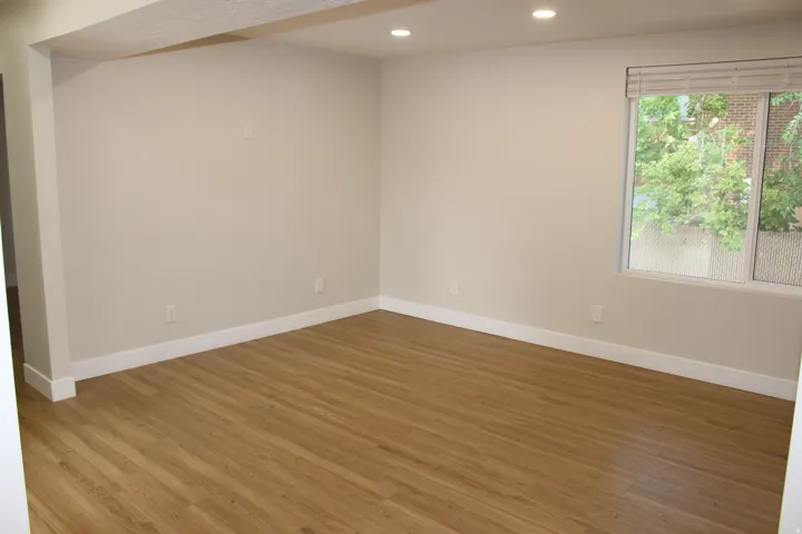 Spacious interior featuring wood-finish flooring, white baseboards, recessed lighting, and a large window with privacy blinds