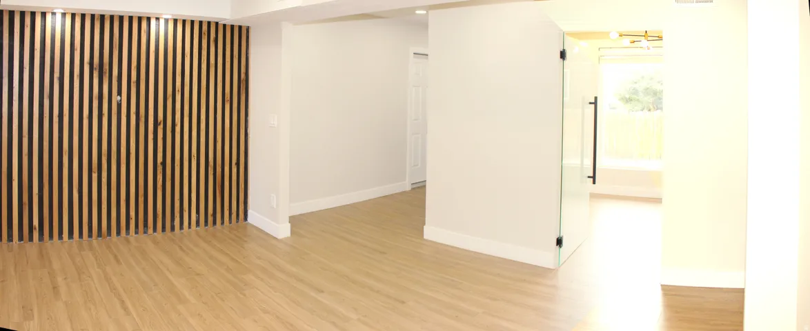 Spacious interior featuring a wood-slat accent wall, light wood-finish flooring, white baseboards, a frameless glass door with a black handle, and recessed lighting