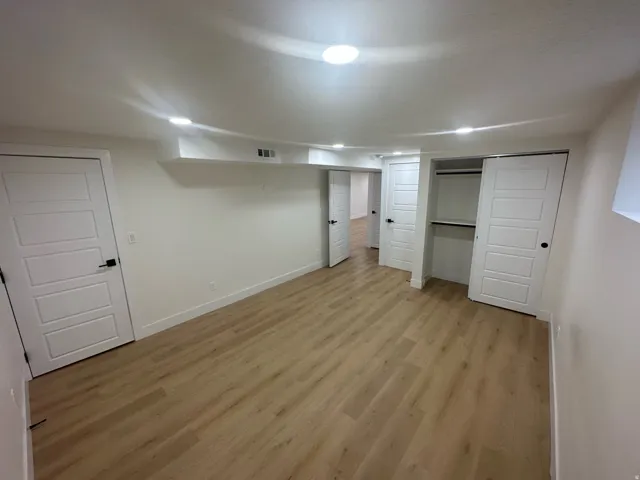 Spacious room, wood-finish flooring, recessed lighting, and white baseboards