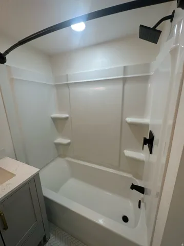 Bathtub and shower combination featuring a white surround, matte black fixtures
