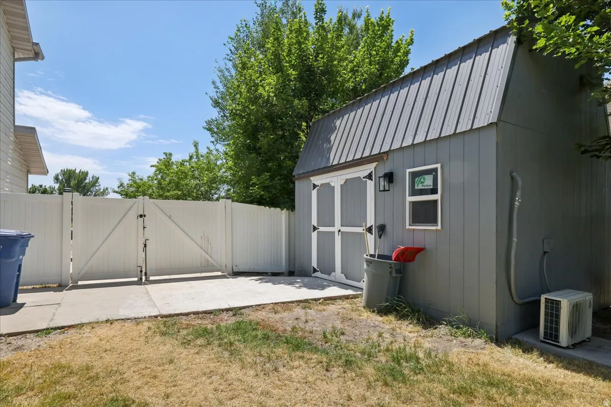 Gray storage shed with a gambrel-style metal roof and white double doors