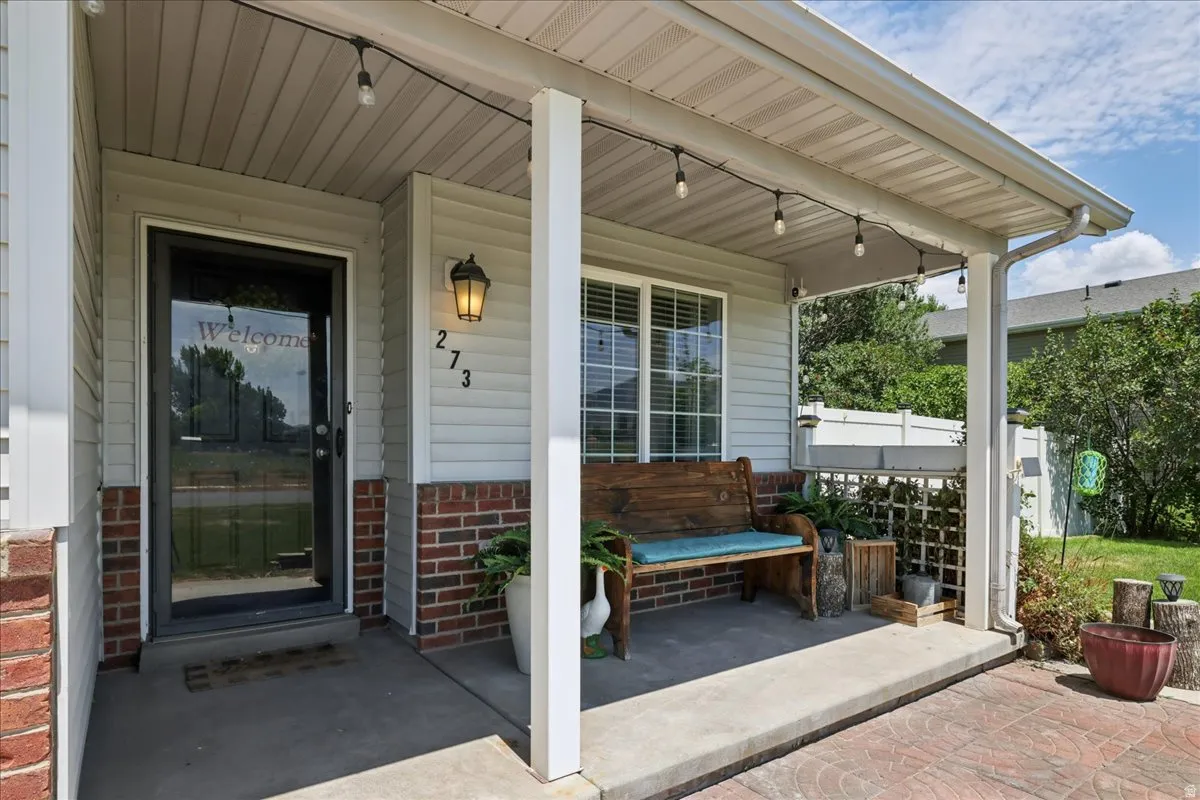 Covered front porch featuring vinyl siding with brick accents, an overhead string lighting fixture, and a concrete patio with a stamped border