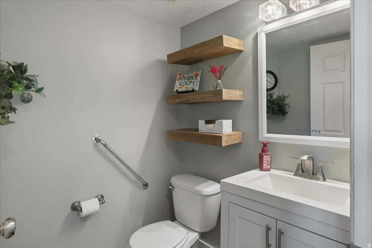 Bathroom featuring a white vanity with integrated sink, a framed mirror with overhead lighting, and three floating wood-finish shelves