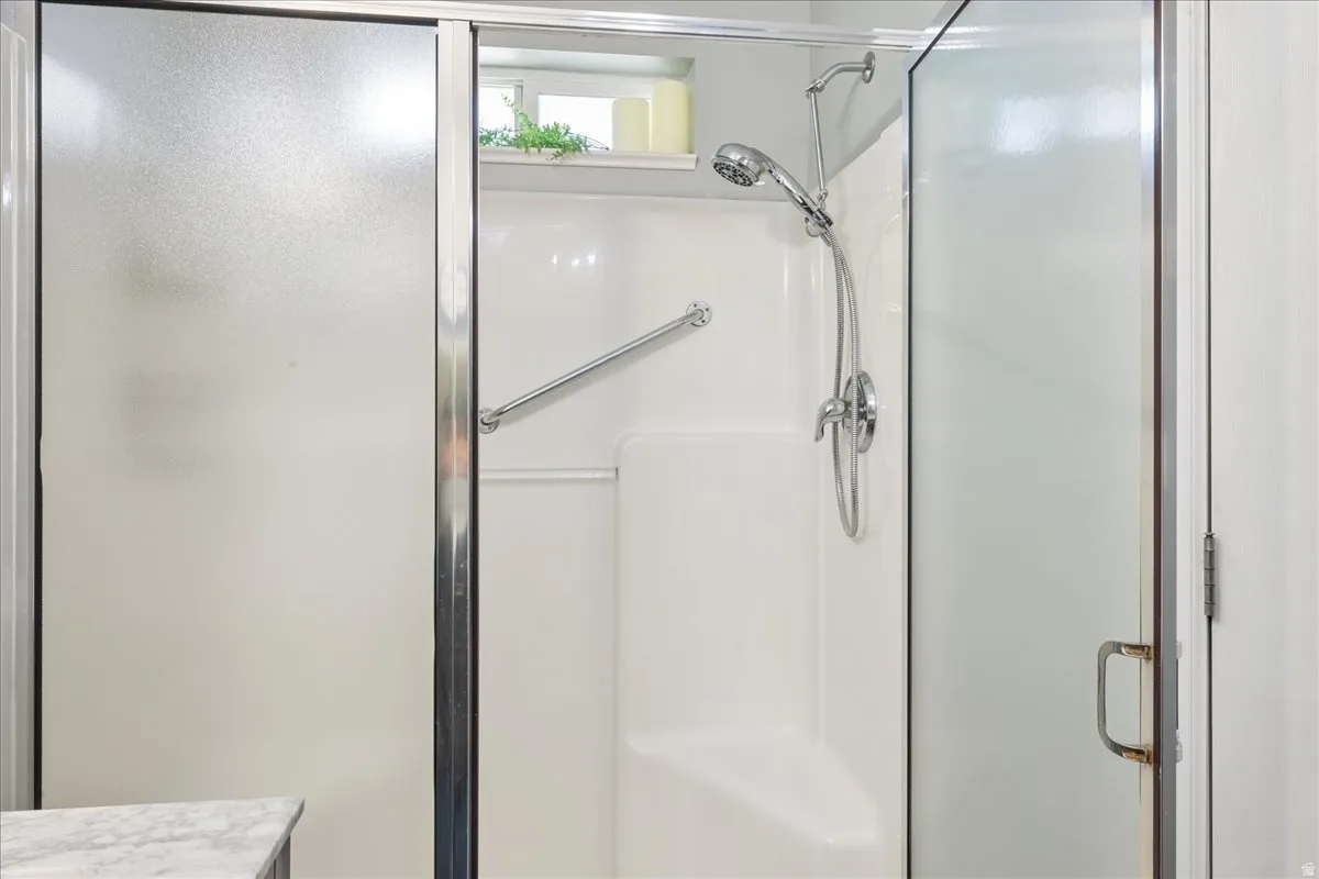 Enclosed shower with frosted glass doors, white composite surround, and a chrome-finish handheld showerhead
