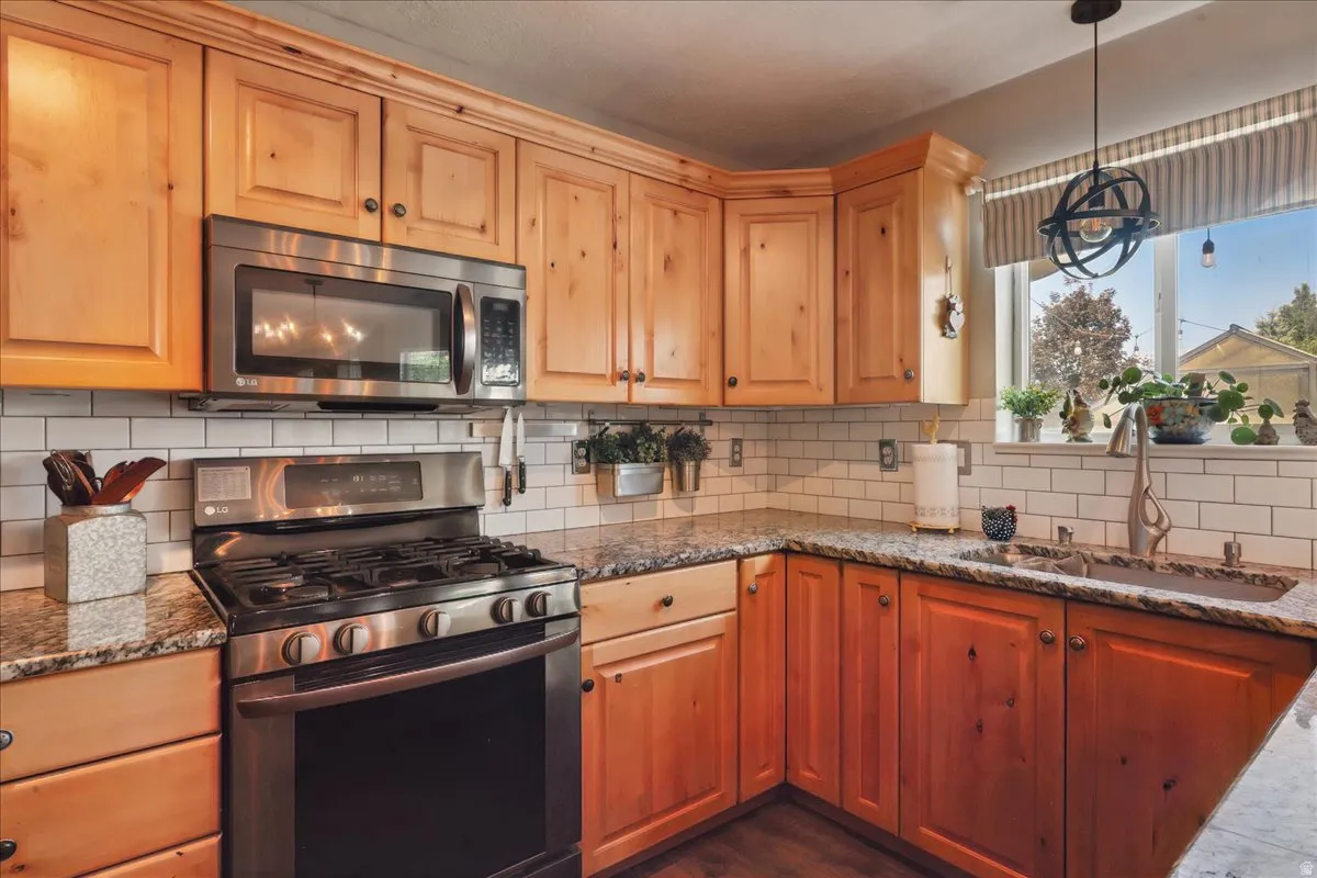 Kitchen featuring light wood cabinetry, stainless steel appliances, granite-style countertops, and a white subway tile backsplash