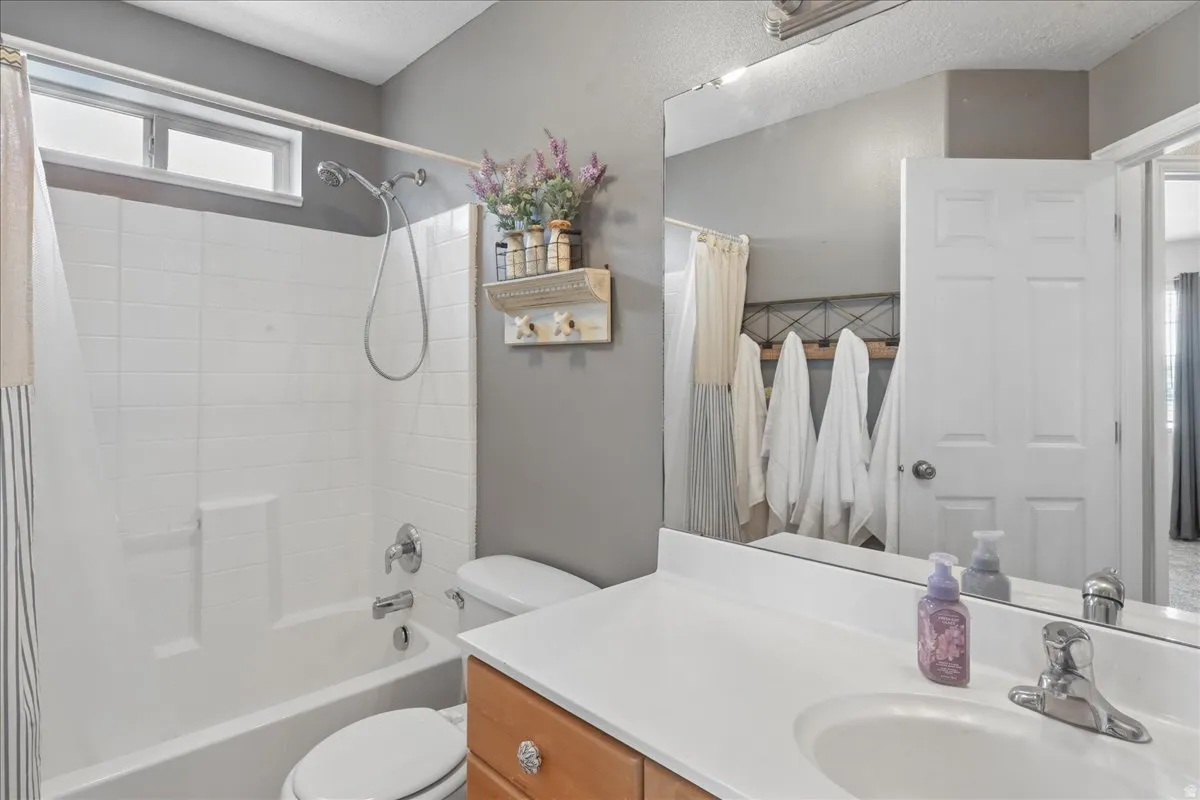 Bathroom featuring a full vanity with a white countertop and integrated sink, a built-in tub with a white tile surround, and a high window for natural light