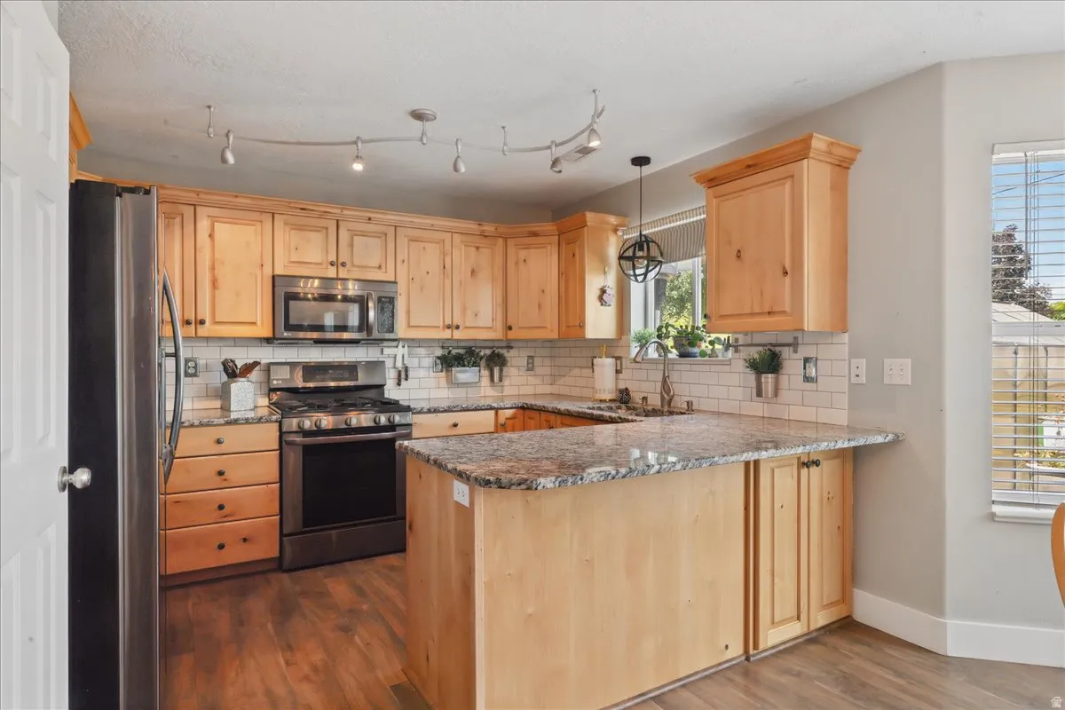 Kitchen featuring wood cabinetry, granite countertops, stainless steel appliances, a subway tile backsplash, and wood-finish flooring