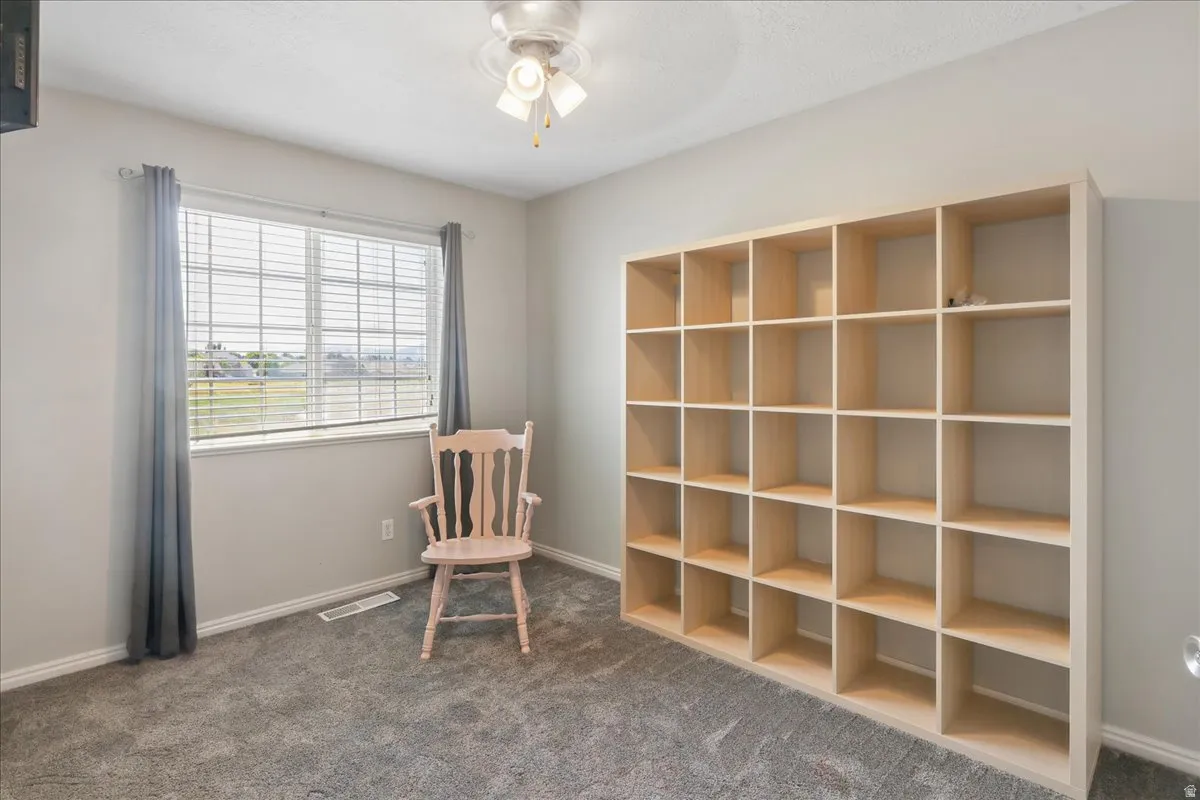 Built-in shelving unit providing extensive storage, complemented by a window with horizontal blinds and a ceiling fan with light fixture