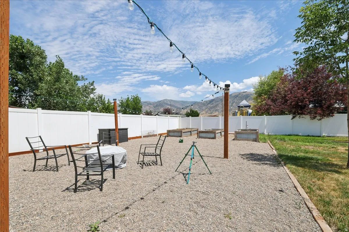 Expansive backyard featuring a white privacy fence, string lighting, and multiple raised garden beds