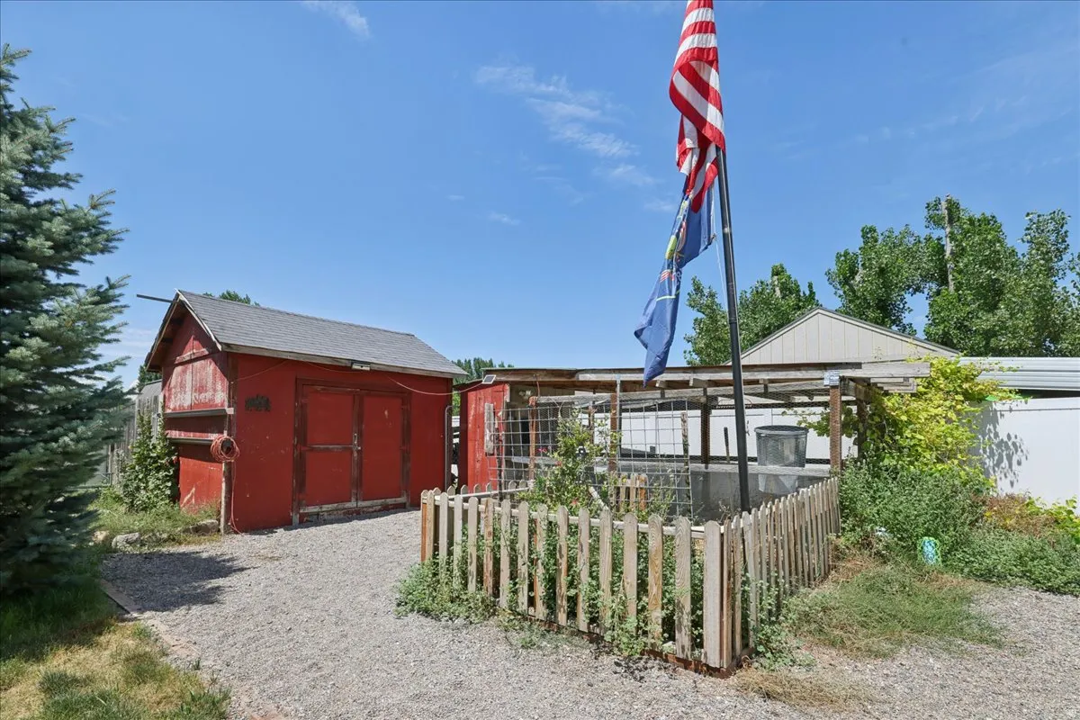 Red utility shed with a gray shingle roof, accompanied by a fenced garden area