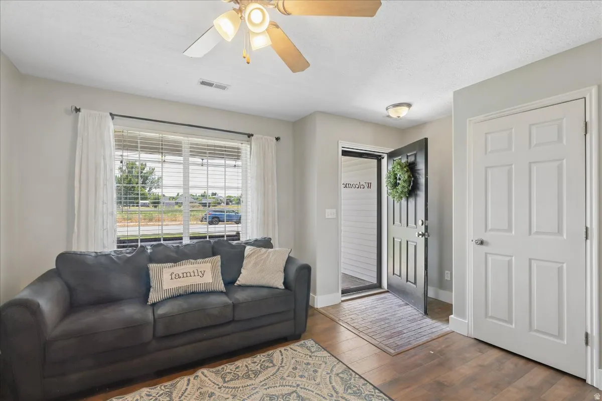 Entryway featuring wood-finish flooring, a contemporary ceiling fan with integrated lighting, a large window with blinds, a six-panel interior door, and light gray wall paint