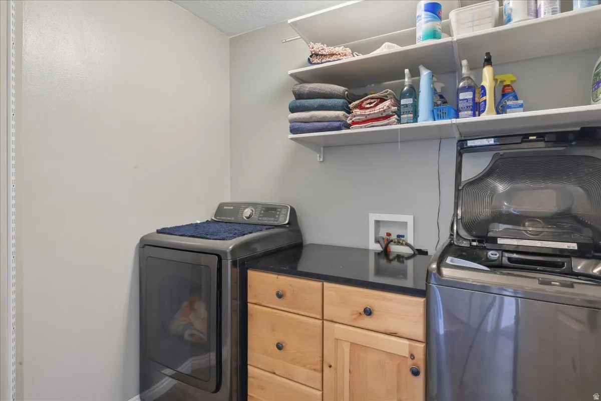 Utility room featuring a built-in wood-finish cabinet with a dark countertop, upper shelving, and a visible washer/dryer hookup