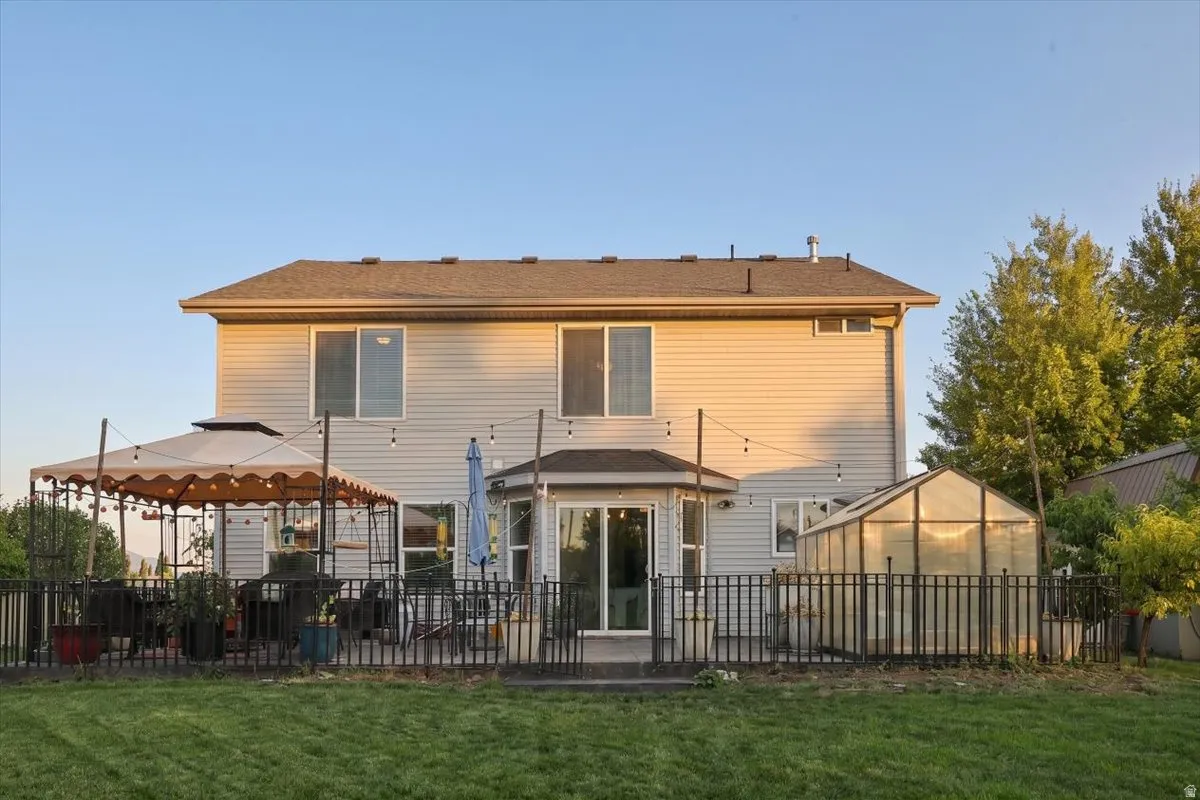 Two-story exterior with siding, a large rear patio, and a fenced-in section featuring a greenhouse