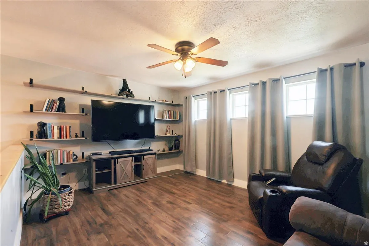 Living area featuring wood-finish flooring, a ceiling fan, multiple windows with neutral drapery, a media console with barn door style fronts, and built-in wall shelving