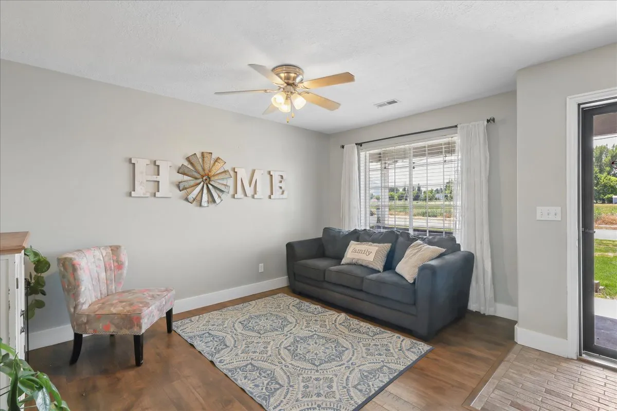 Spacious living area featuring wood-finish flooring, a ceiling fan, and a large window with blinds