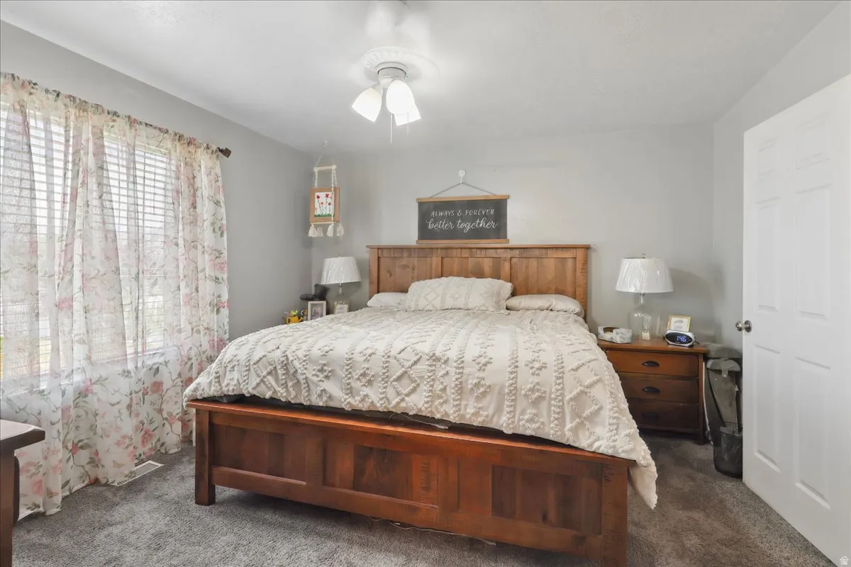 Carpeted bedroom featuring a window with blinds, a ceiling fan, and a paneled door