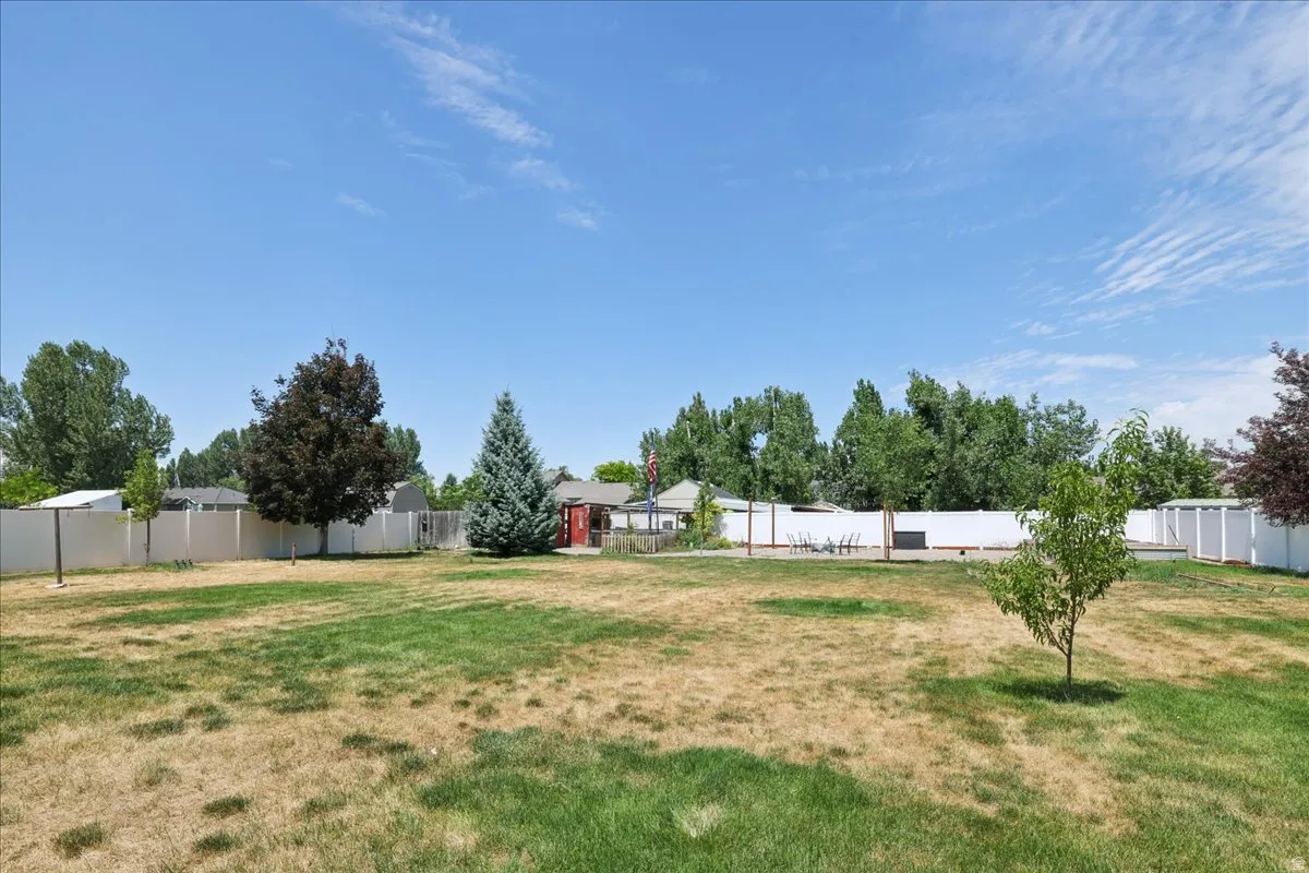 Expansive outdoor space featuring a white privacy fence, mature trees, a garden shed, and a dedicated patio area