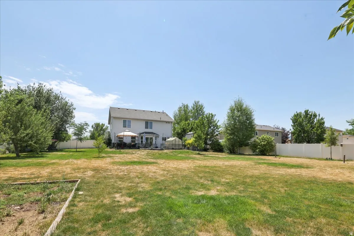 Expansive backyard featuring a large lawn, mature trees, and a white privacy fence