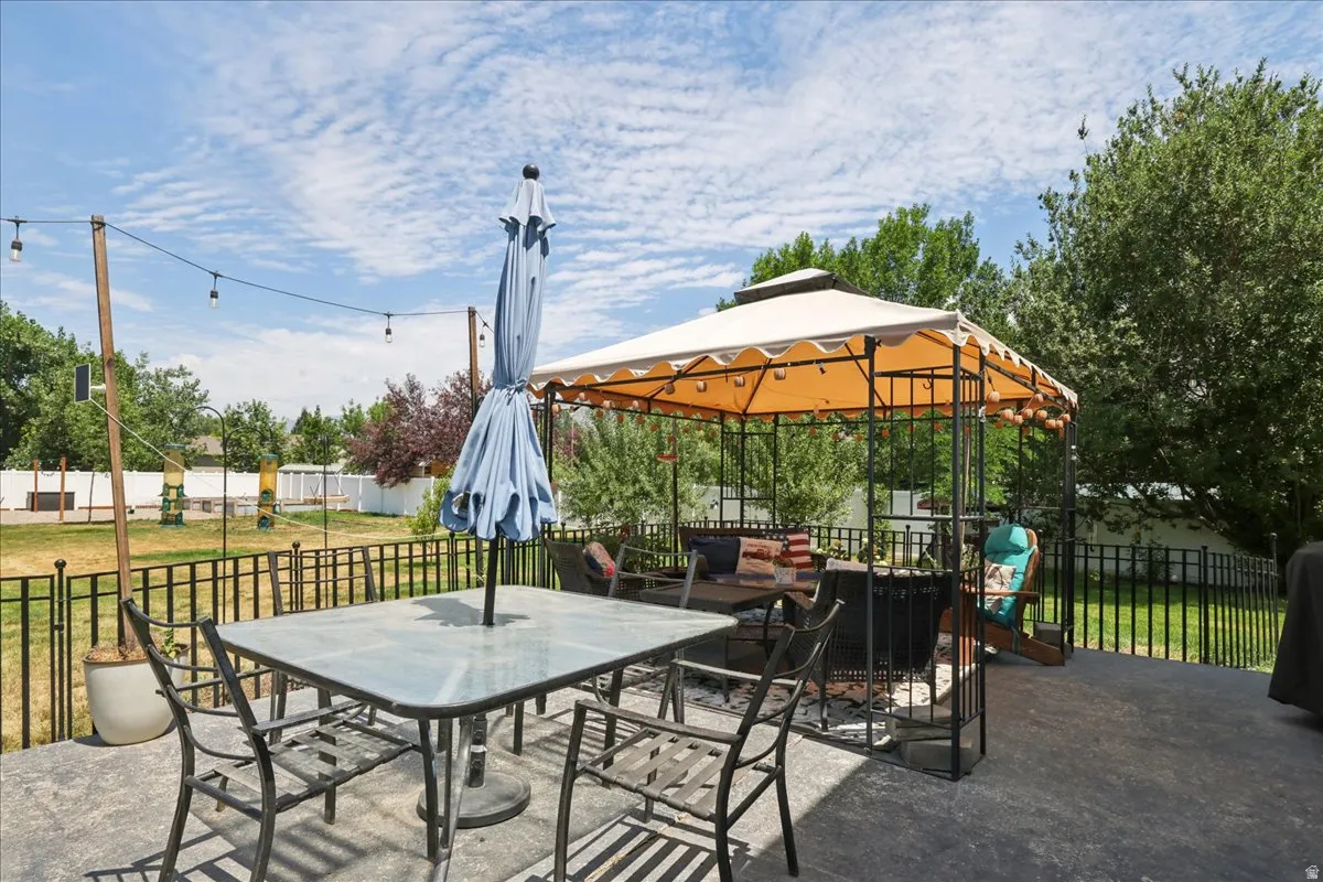 Spacious concrete patio featuring a metal gazebo, string lighting, and a black wrought iron fence