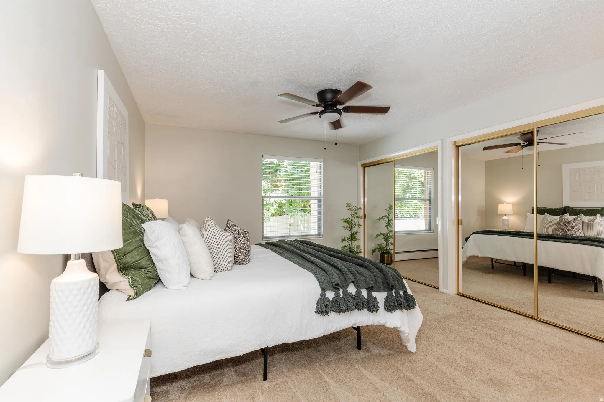 Carpeted bedroom with a ceiling fan, window with blinds, and mirrored sliding closet doors