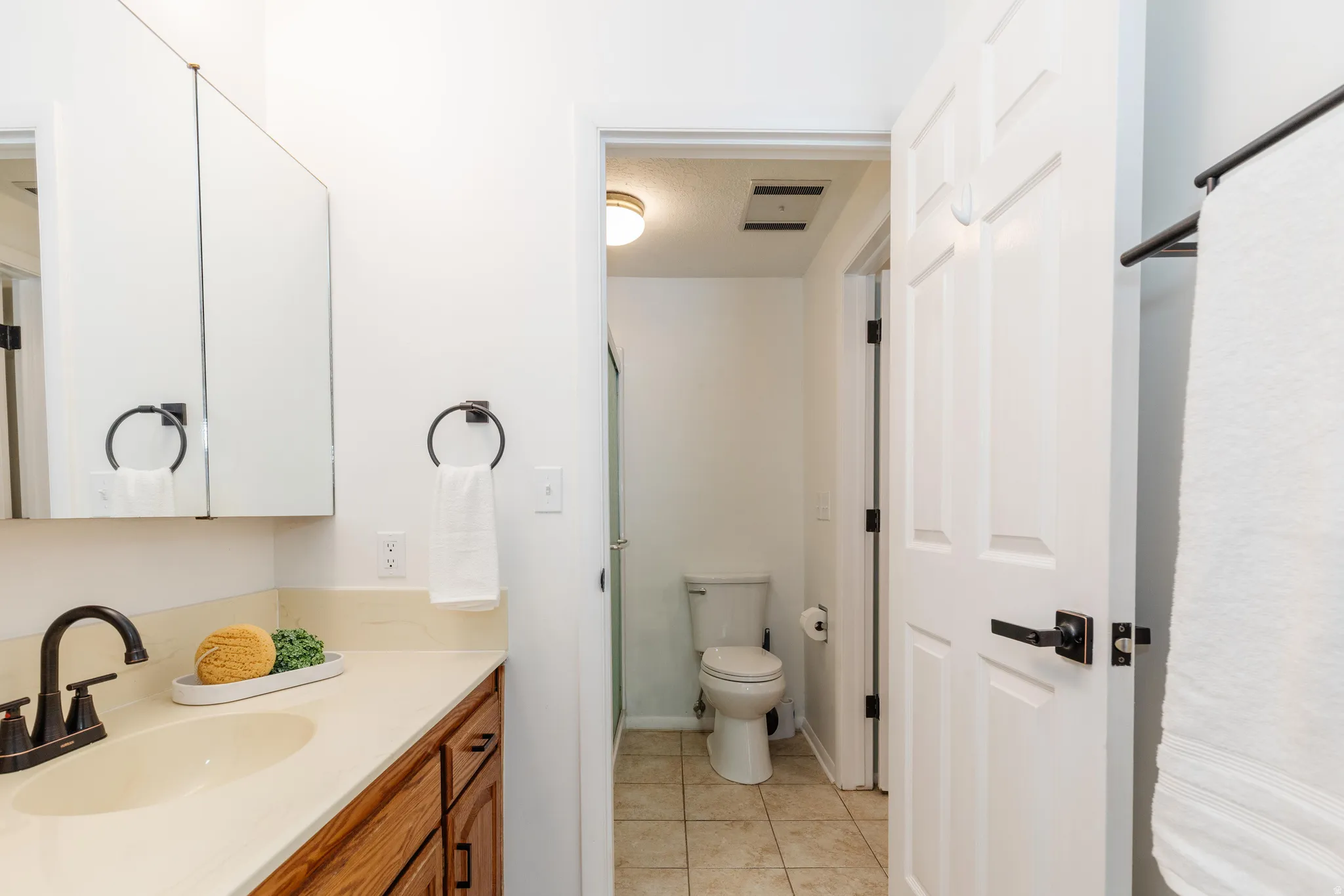 Bathroom vanity featuring wood cabinetry, a light-toned countertop, and a built-in oval sink with a matte black faucet