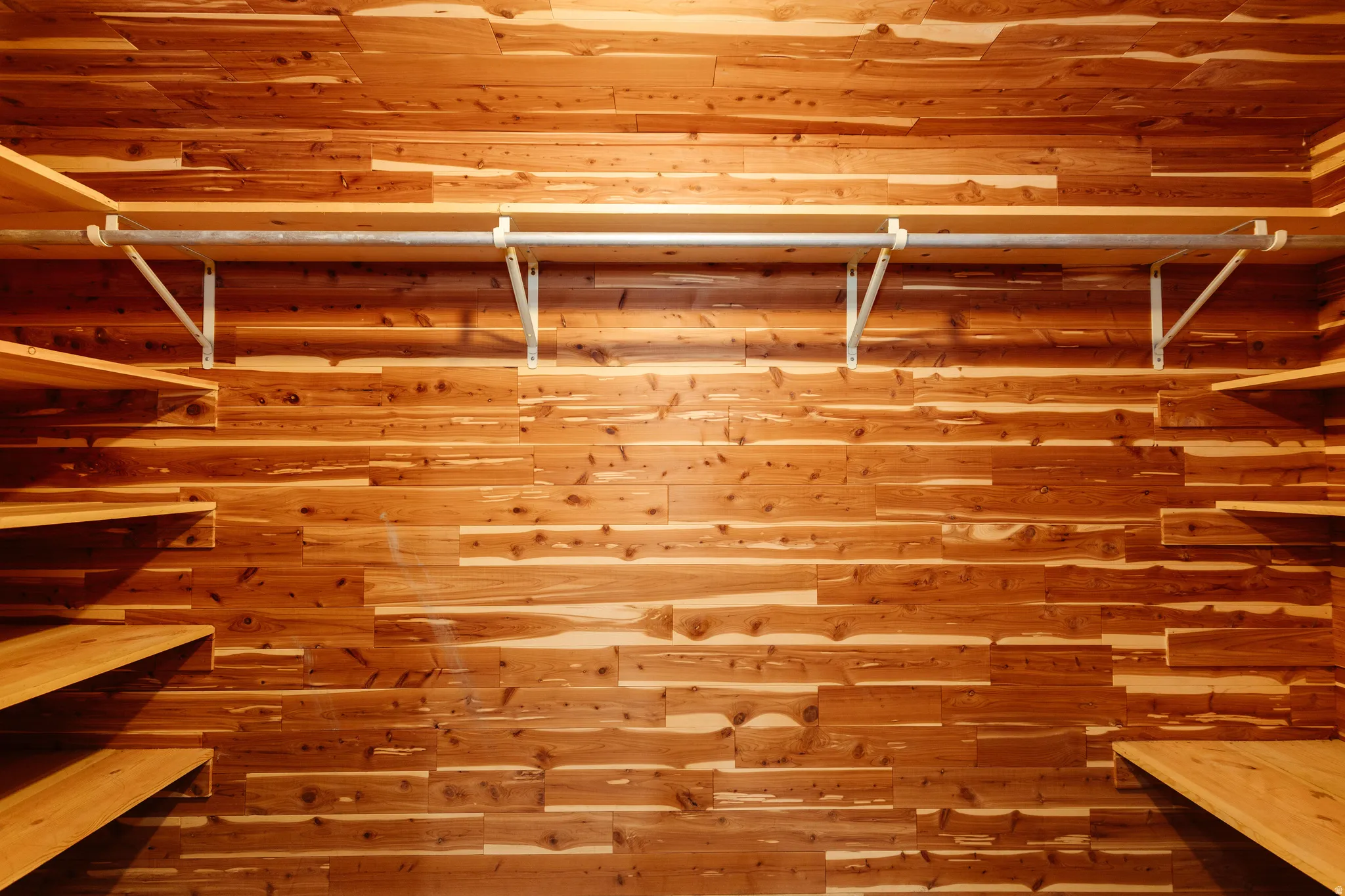 Custom-built closet featuring cedar plank wall finishes, integrated shelving, and a metal hanging rod with sturdy supports