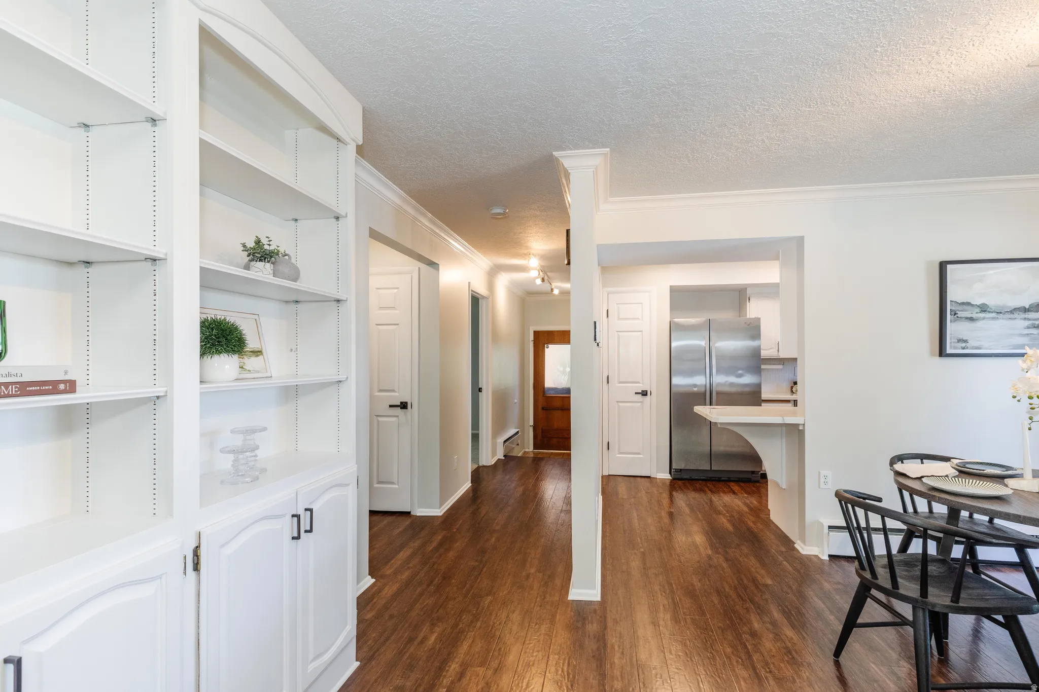 Built-in white shelving with lower cabinetry, wood-finish flooring, white crown molding, recessed lighting, and a kitchen featuring stainless steel appliances