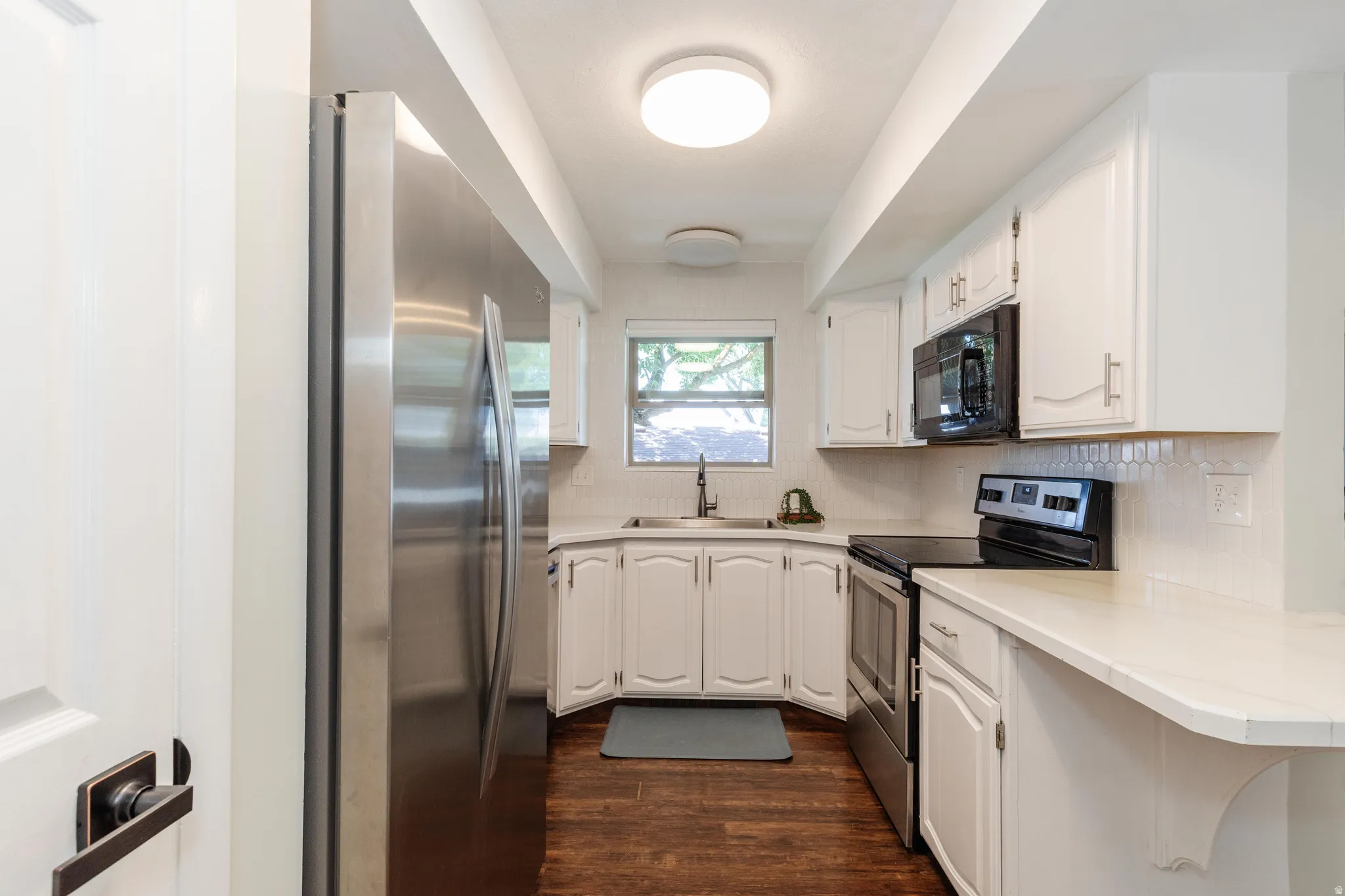 Compact kitchen featuring white cabinetry, stainless steel appliances, light-toned countertops, a white tile backsplash, and wood-finish flooring