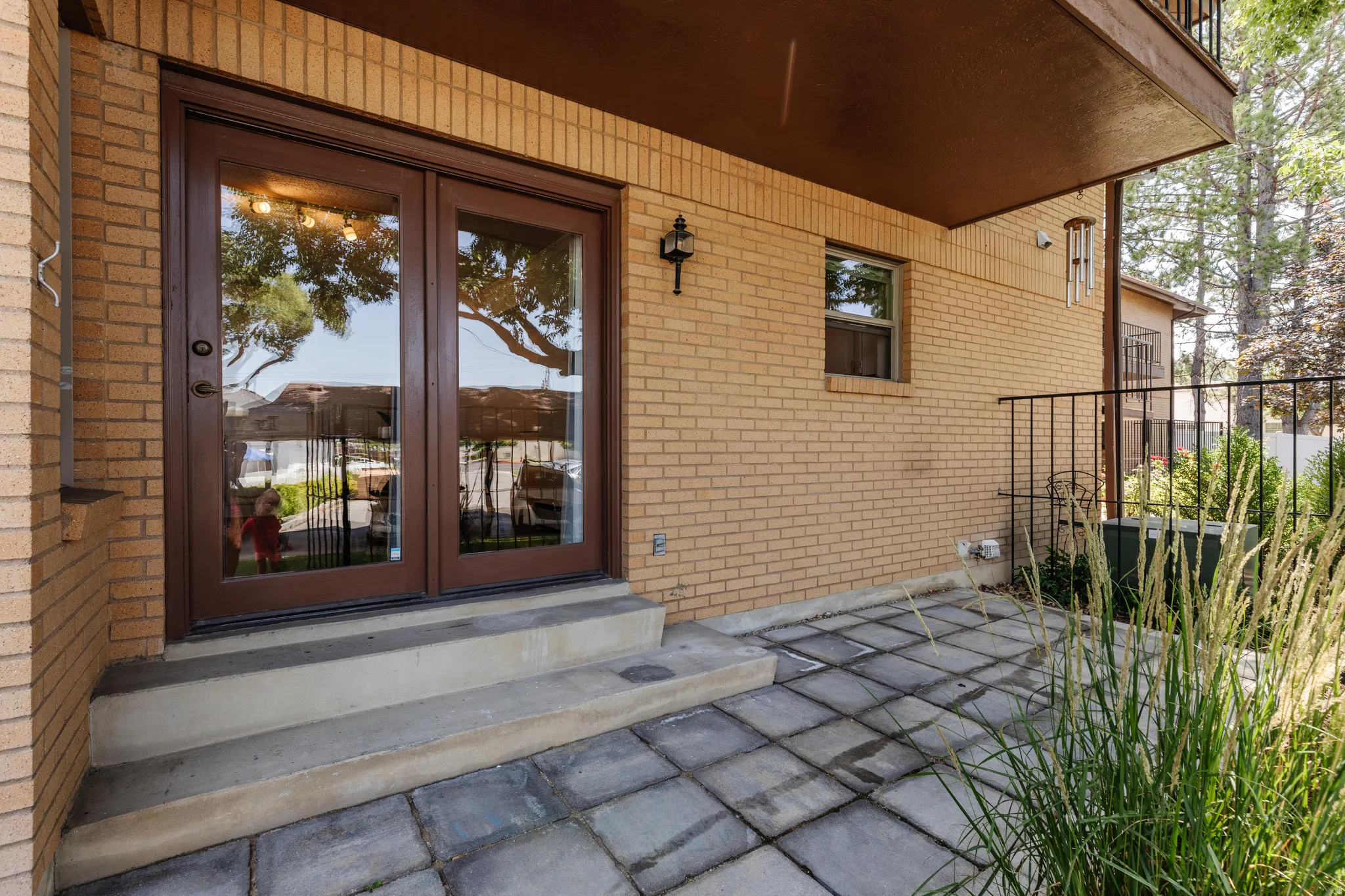 Brick exterior featuring a private patio with concrete paver stones, double glass-paneled doors, and an overhead balcony