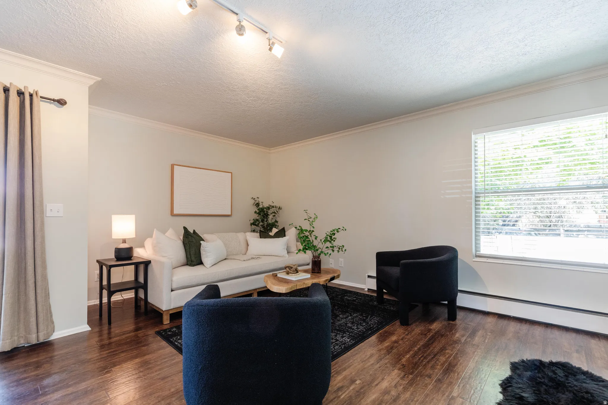 Living space featuring wood-finish flooring, crown molding, a large window with blinds, and track lighting