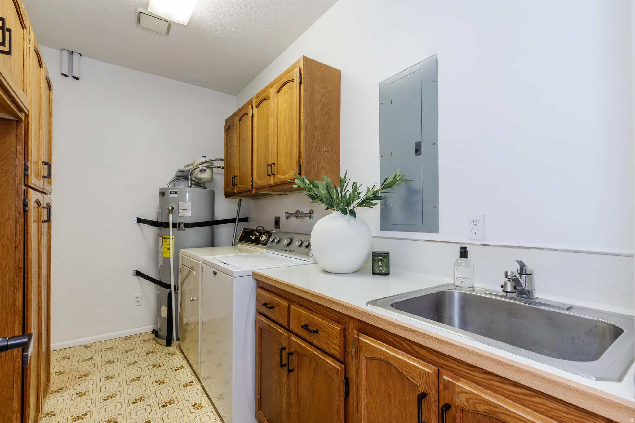 Utility room featuring wood cabinetry, laminate countertops, a stainless steel sink with a chrome faucet, and patterned vinyl flooring