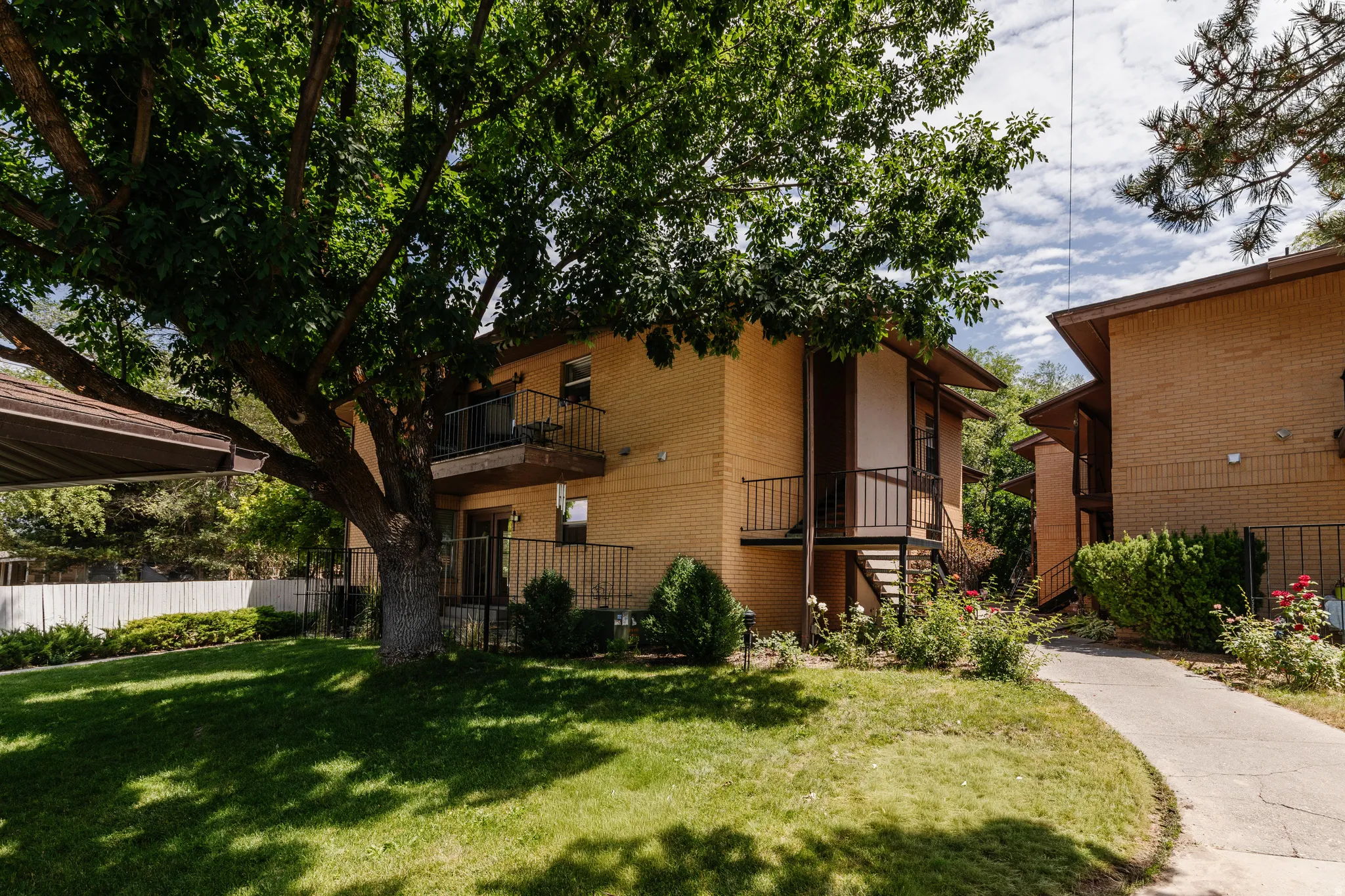 Exterior brick building with individual balconies, a covered outdoor area, and a large mature tree