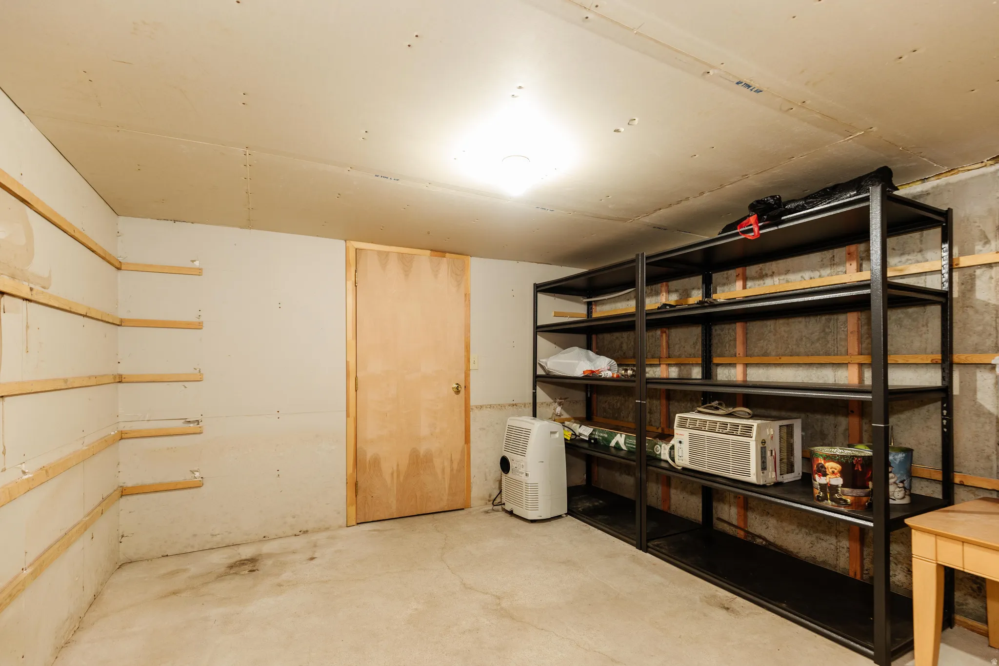 Spacious storage area featuring concrete flooring, a natural wood door, and a prominent metal shelving unit with multiple tiers
