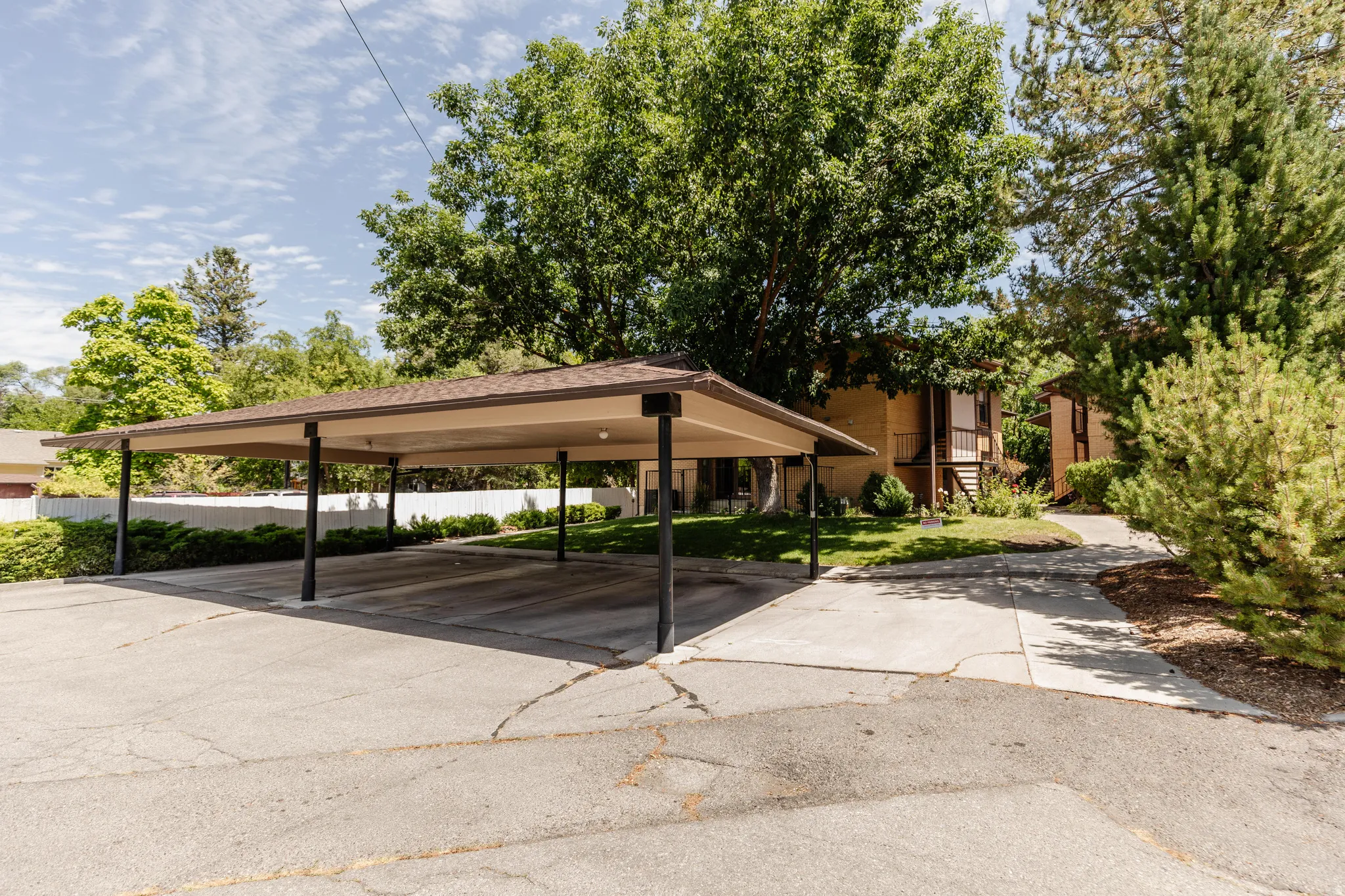 Covered parking structure with multiple bays, asphalt surface, and surrounding mature trees and landscaping