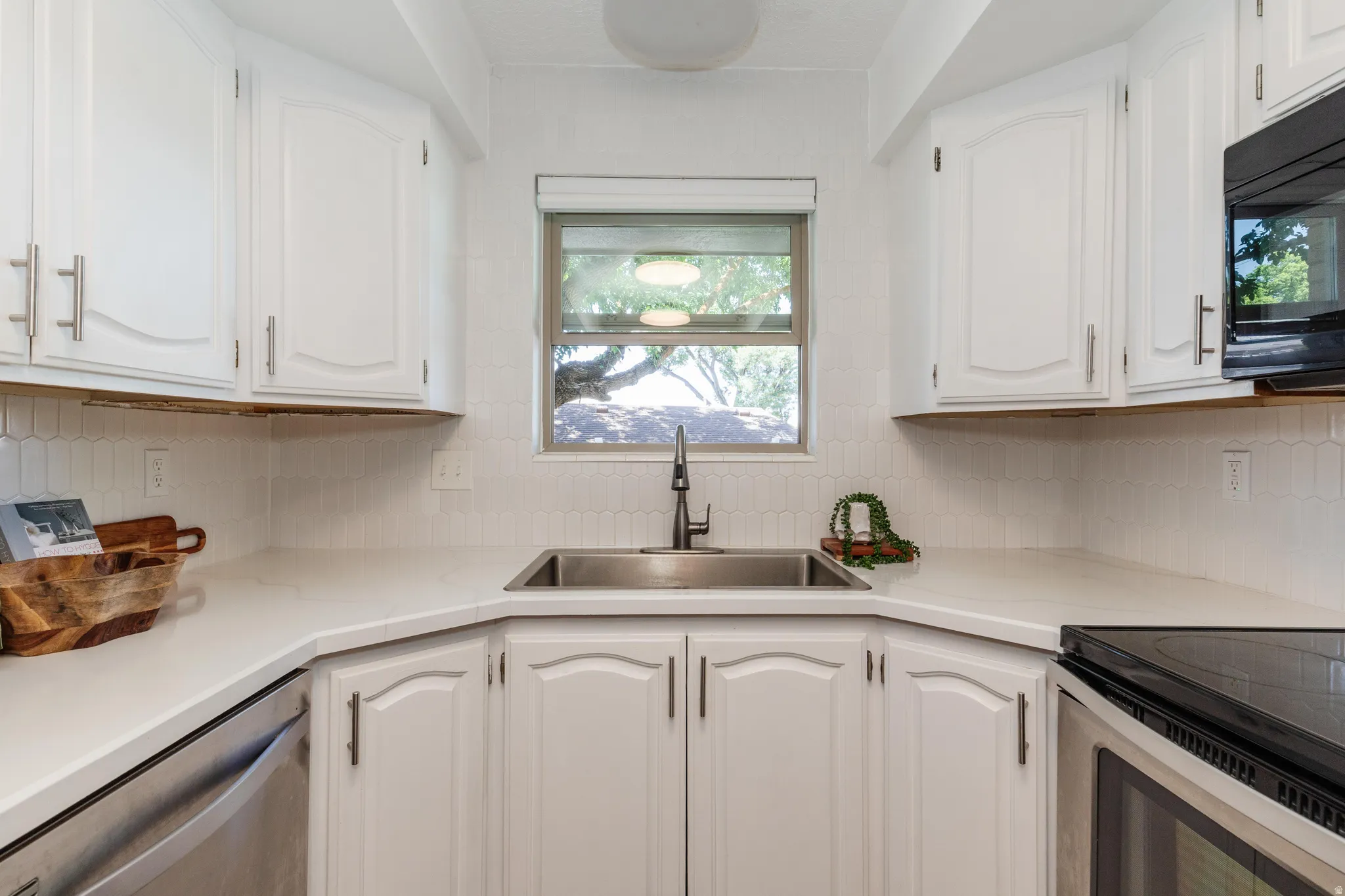 Kitchen featuring white cabinetry, light-toned countertops, a stainless steel sink with a dark-finish faucet, and a white tile backsplash